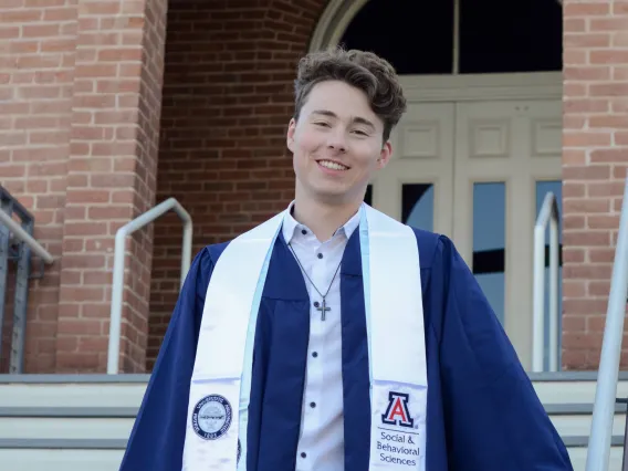 person in graduation regalia pictured in front of old main