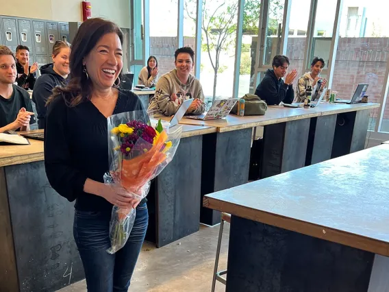 woman smiling holding flowers with smiling students in the background