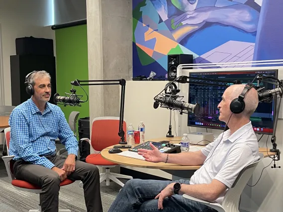 two men sitting in front of technical gear speaking into mics