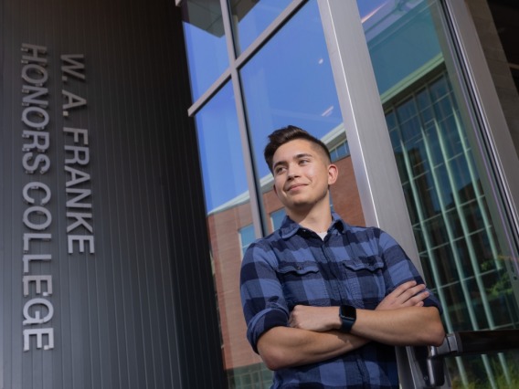 student with crossed arms standing in front of sign that reads W.A. Franke Honors College
