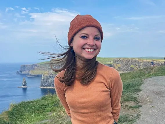 student standing in front of green hills wearing orange