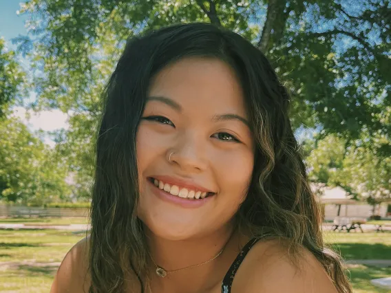 student sitting in front of green grass and trees