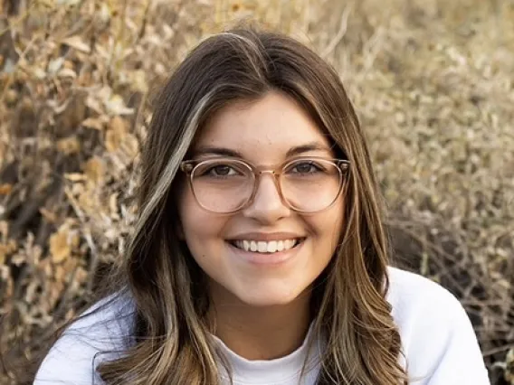 woman sitting in a field wearing white University of arizona shirt and jeans