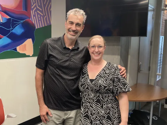 John Pollard and Jacqueline Melvold standing in podcast studio smiling for camera