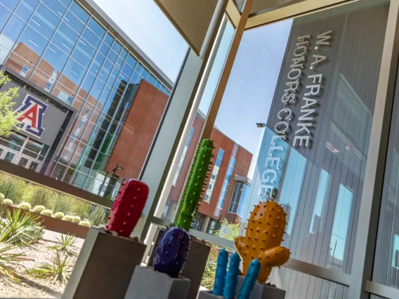 view facing outside of a window with metal cactus installment, words W.A. Franke Honors College in metal writing on outside of building