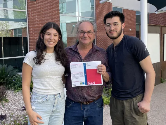 three people smiling one holding a play Red brick wall background