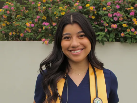 woman standing in front of flowers with yellow stole and nursing scrubs