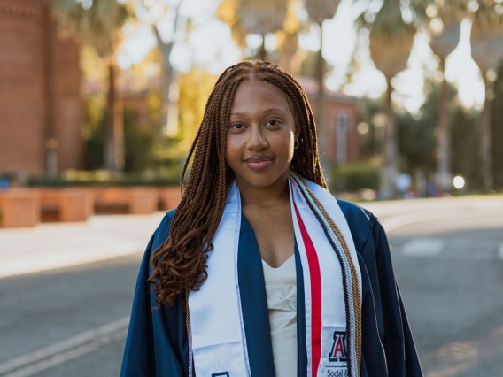 graduate standing in road wearing blue regalia and white stole