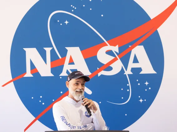 dante lauretta speaking with microphone in front of NASA sign