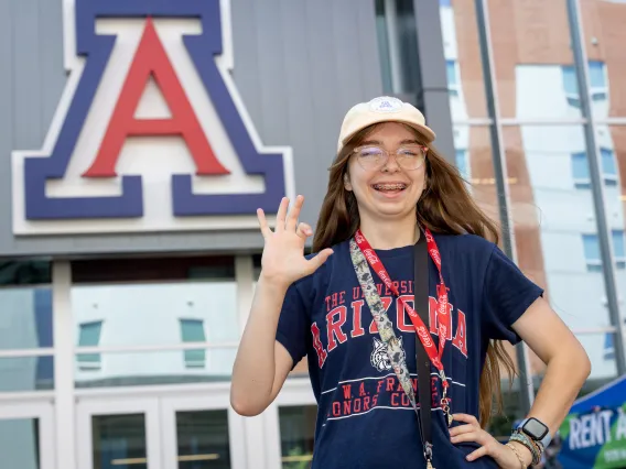 student in front of block A showing wildcat hand gesture