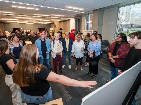 student presenting work to a group of people gathered around a poster
