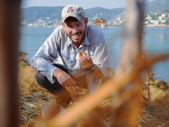 person crouching down holding rock, blue lake background