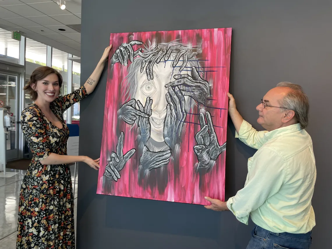 Rachel Newcomb and Patrick Baliani putting up Necomb's self portrait in the Poetry center