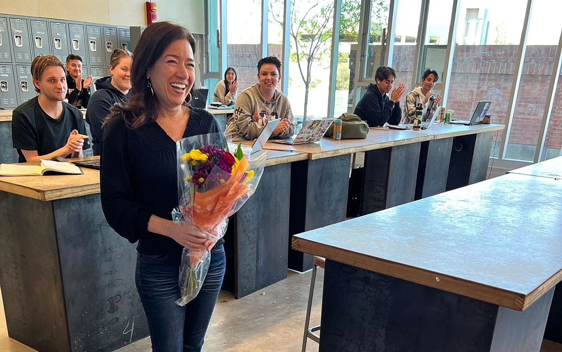 woman smiling holding flowers with smiling students in the background