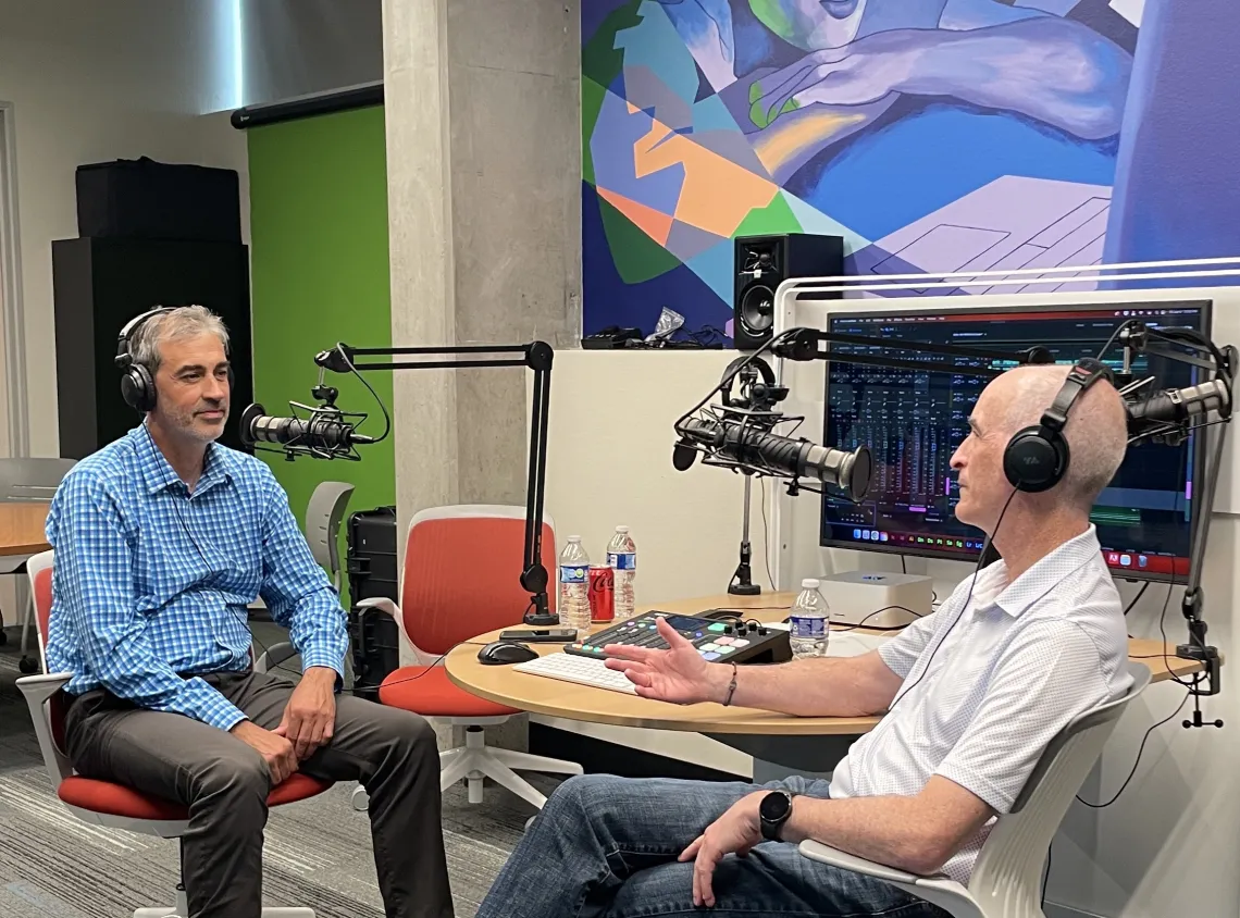 two men sitting in front of technical gear speaking into mics