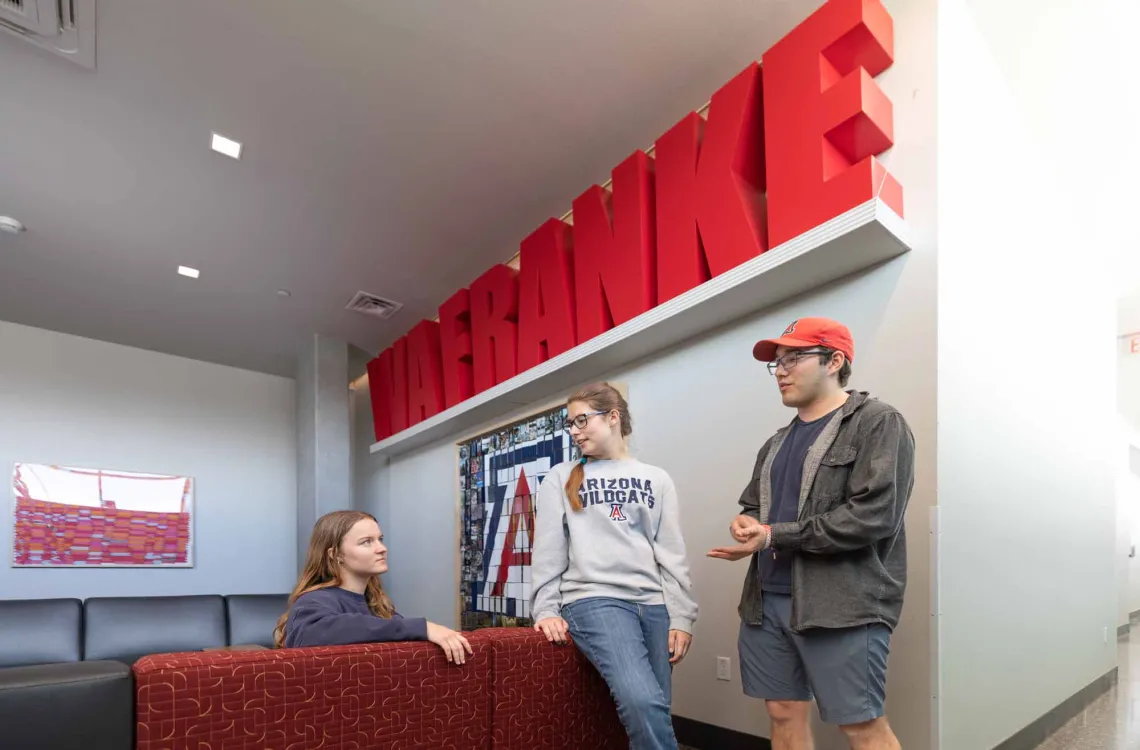 Picture shows three students talking in the Living Room area of the Honors Village Dorm.