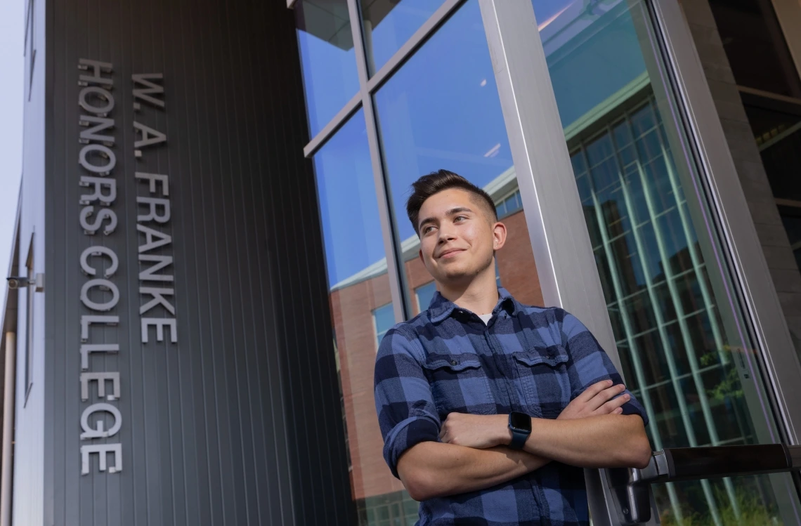 student with crossed arms standing in front of sign that reads W.A. Franke Honors College