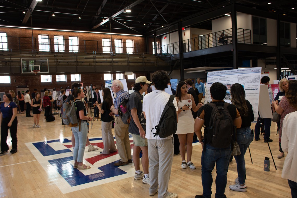 Photo shows W.A. Franke Honors students explaining their research project to other students and faculty in Bear Down Gym.