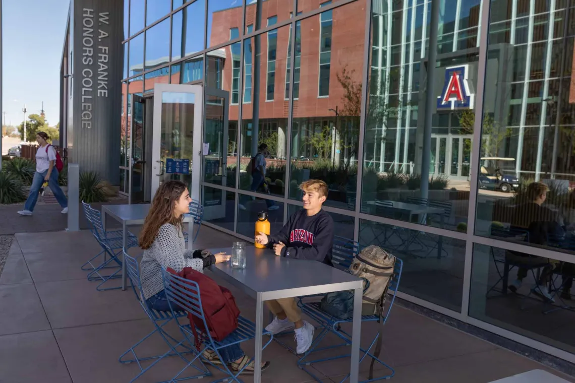 Two students sitting outside the entrance to the W.A. Franke Honors Village