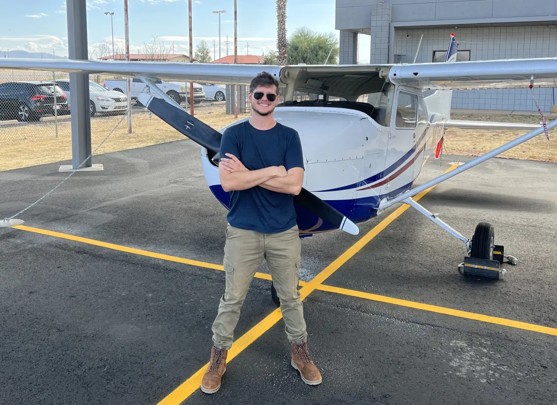 man standing with arms crossed in front of small propeller plane 