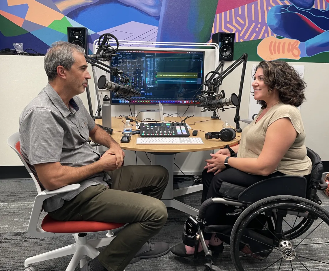 a man and a woman sitting in front of technical gear speaking into mics