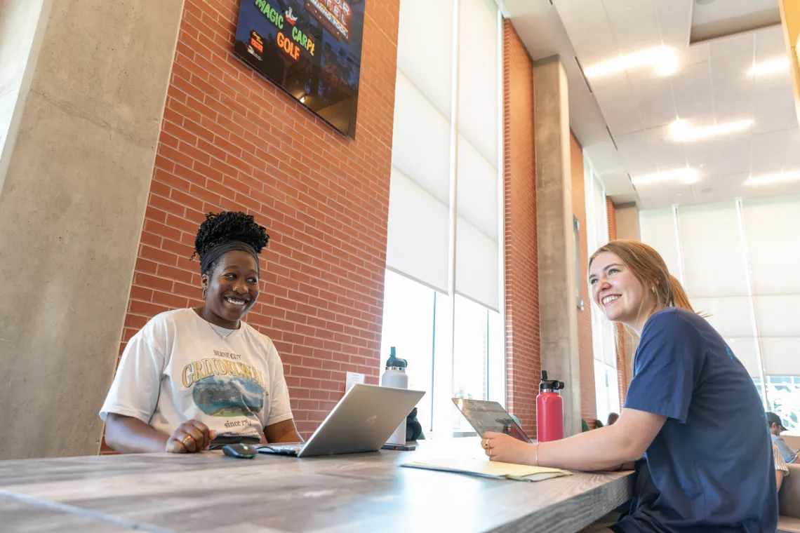 two women looking at camera sitting across from each other in lobby