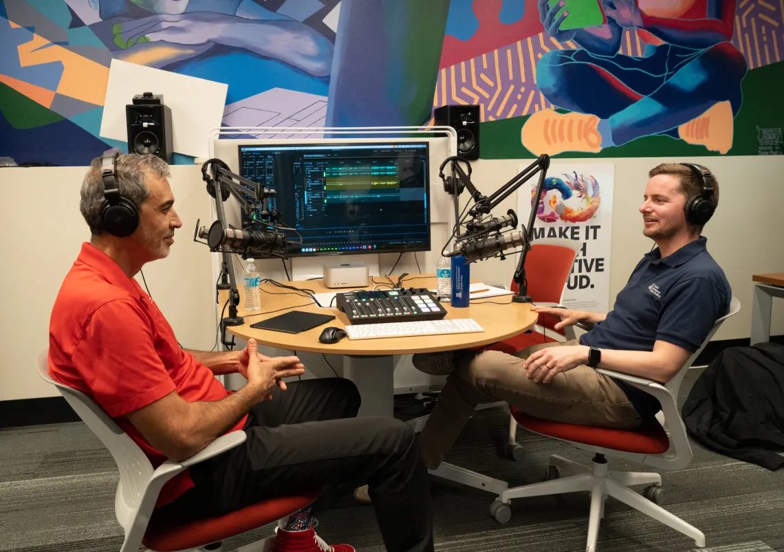 two men sitting in front of technical gear speaking into mics