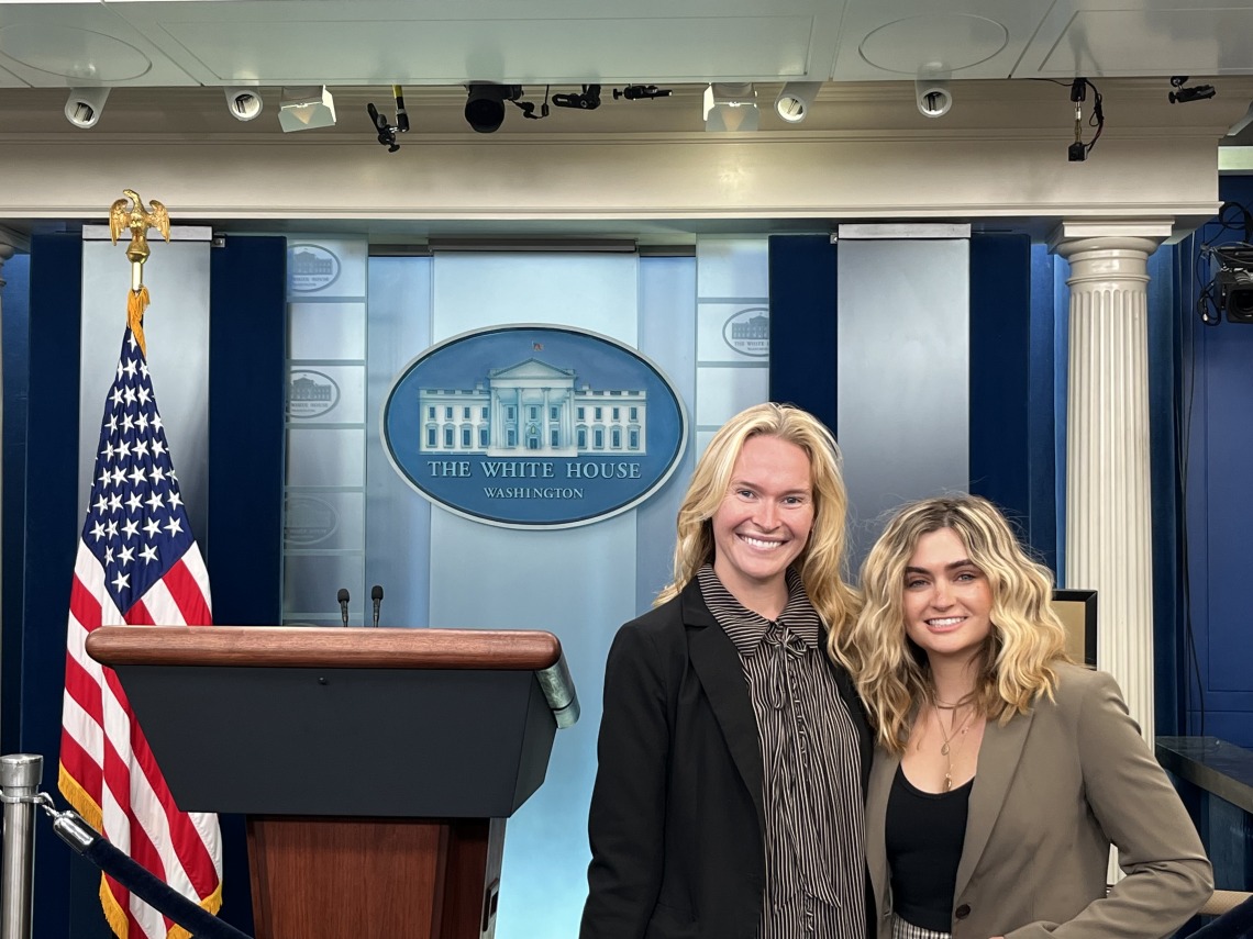 two women standing with white house background 