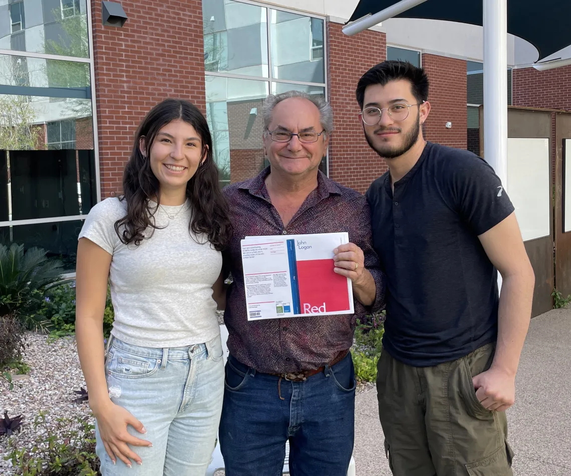 three people smiling one holding a play Red brick wall background