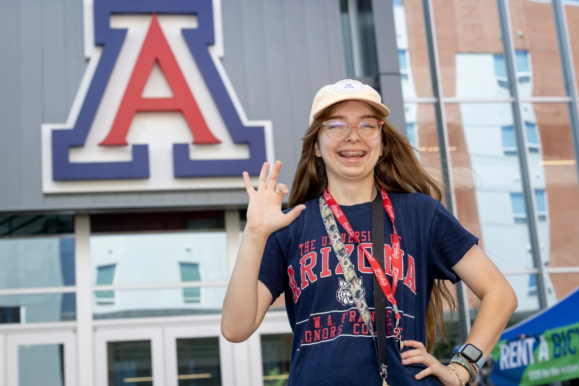 student in front of block A showing wildcat hand gesture