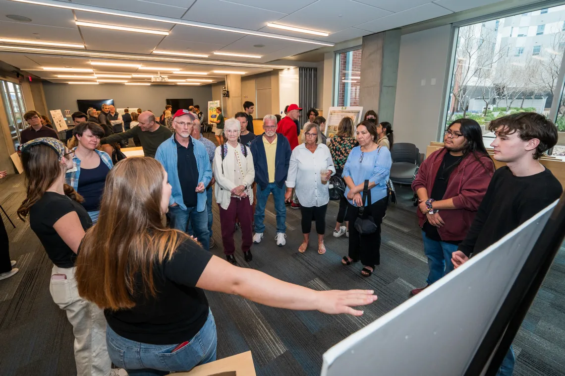student presenting work to a group of people gathered around a poster