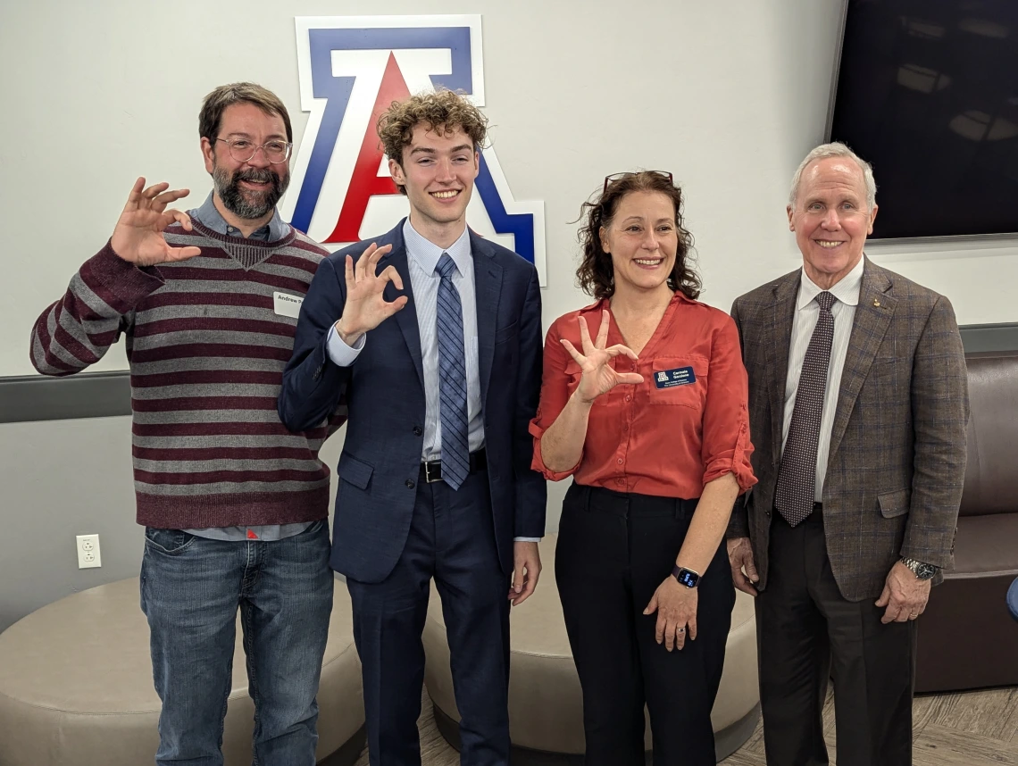 four people showing wildcat hand symbol pictured in front of University of Arizona Block A