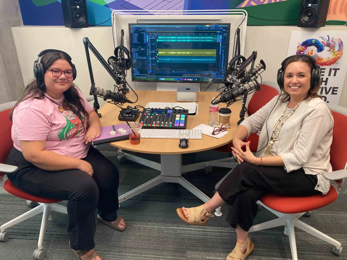 two people smiling in front of podcast equipment