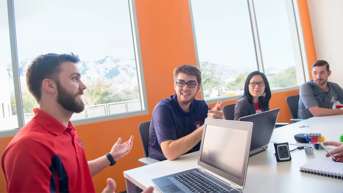 Four students around a table talking.