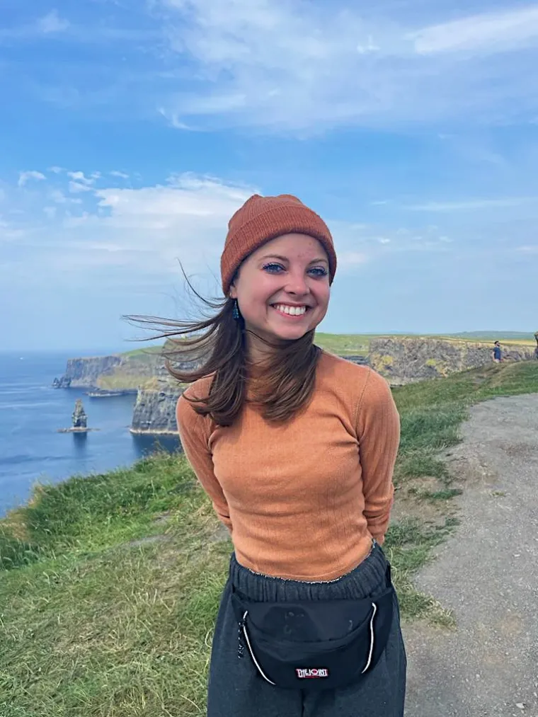 student standing in front of green hills wearing orange