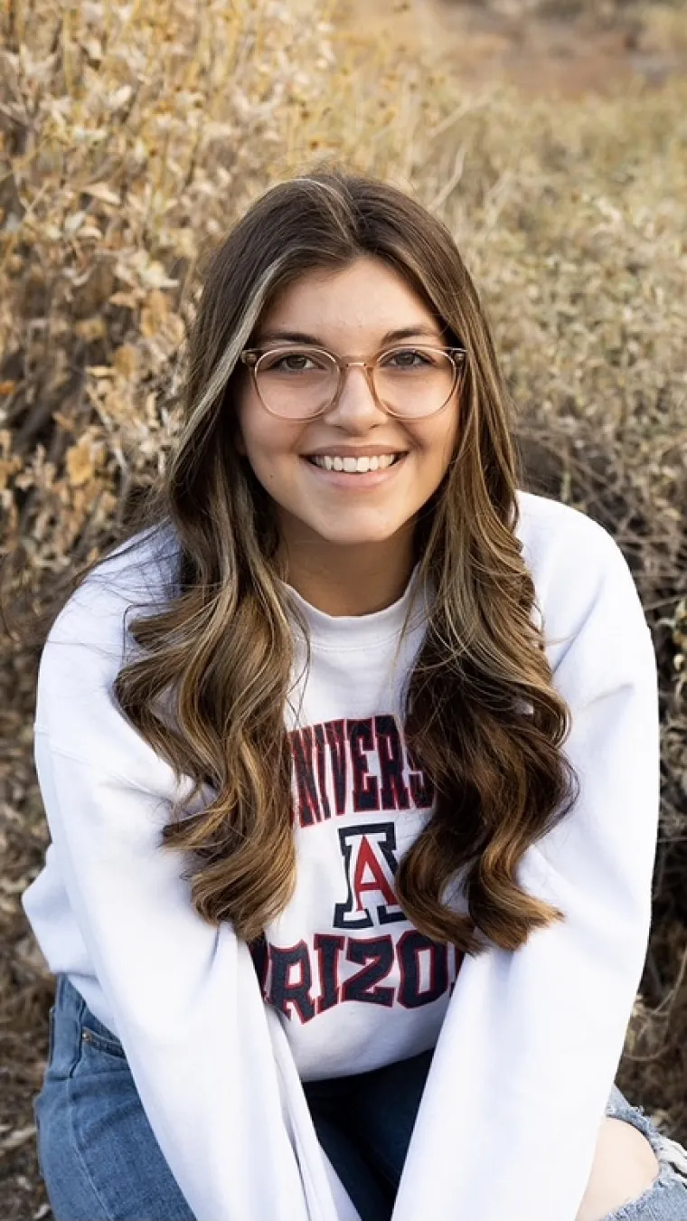 woman sitting in a field wearing white University of arizona shirt and jeans