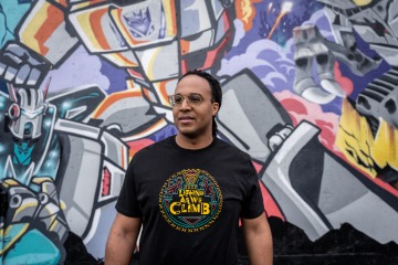 Joel Harris, Graffiti background, black shirt with yellow green red design "Lifting as we climb"