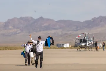 person walking away from helicopter with bucket and arms raised in celebration