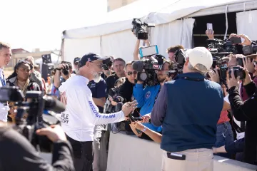 person speaking to reporters by tent