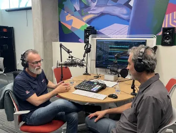 two men sitting in front of technical gear speaking into mics