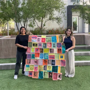 two students holding colorful tapestry