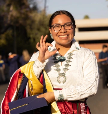 student showing wildcat hand sign wearing native american regalia