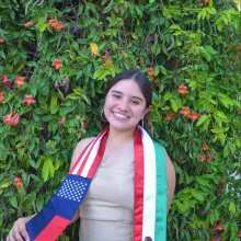 woman in front of green background wearing graduation regalia