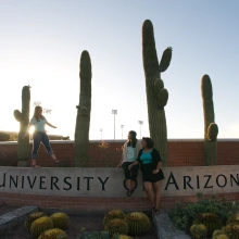 Students on stone UA sign at Campbell & 6th St.