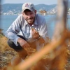 person crouching down holding rock, blue lake background